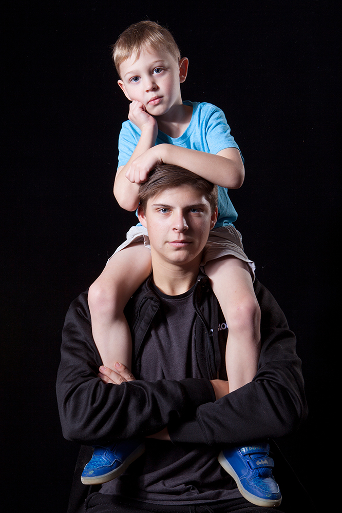 studio photo of teenager and younger sibling sitting on his shoulders